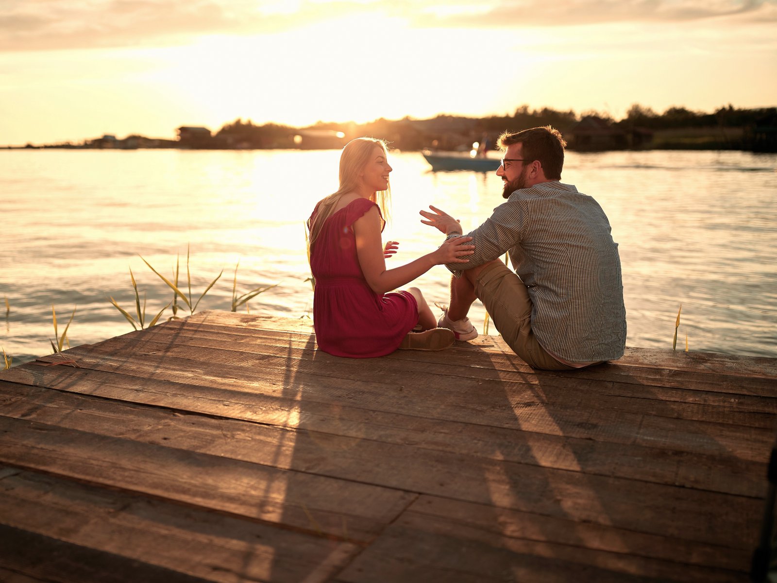 Zwei Menschen sitzen bei Sonnenuntergang am Wasser und sprechen ruhig miteinander