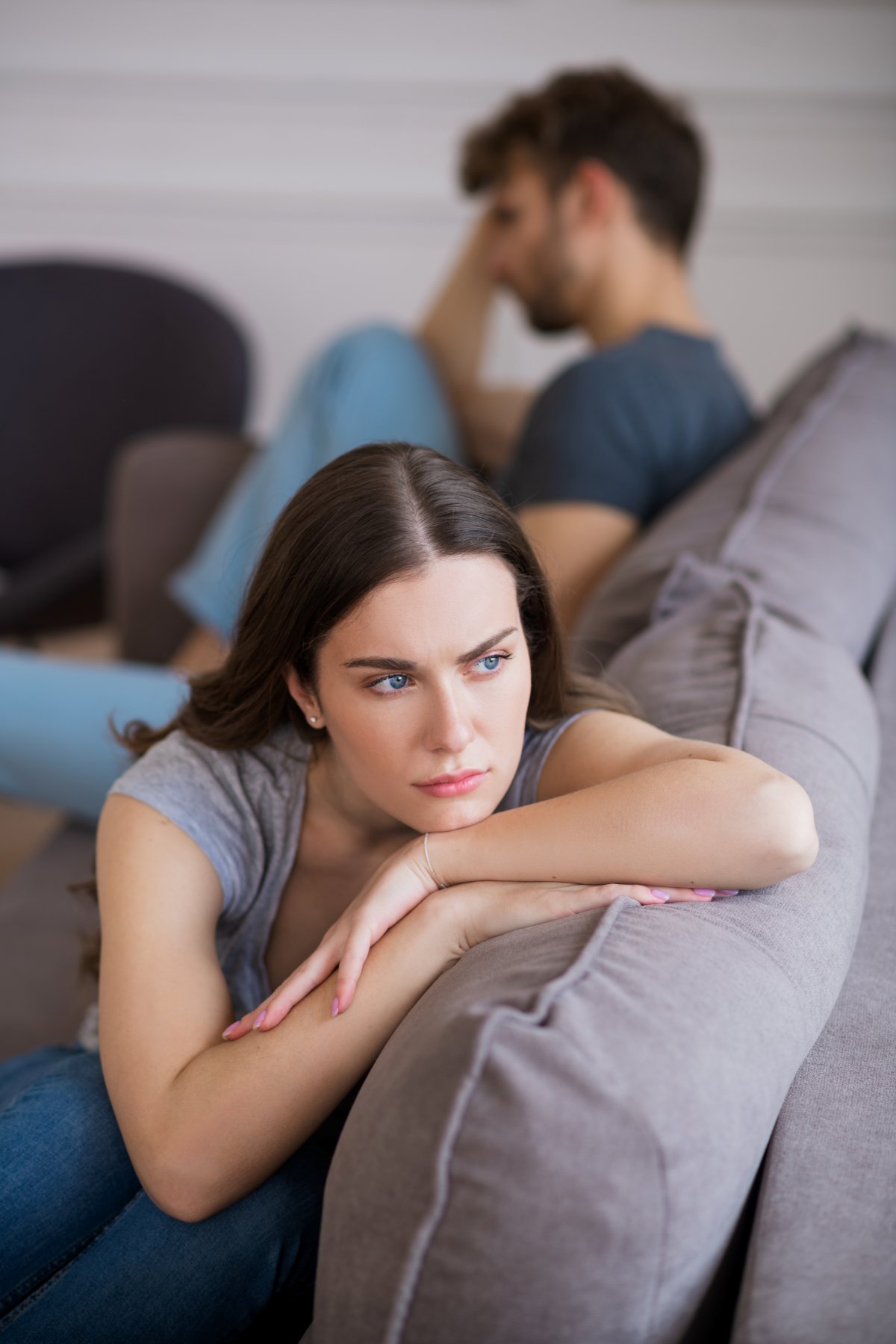 Nachdenkliche Frau im Vordergrund, Mann im Hintergrund – emotionale Distanz. Konflikte klären in einer Beziehung