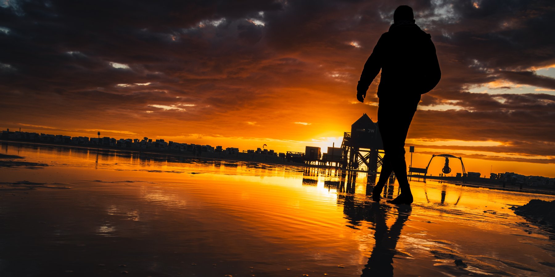 Silhouette eines Mannes am Strand bei Sonnenuntergang mit Spiegelung im Wasser