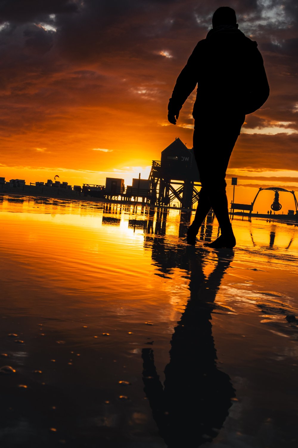 Silhouette eines Mannes am Strand bei Sonnenuntergang mit Spiegelung im Wasser