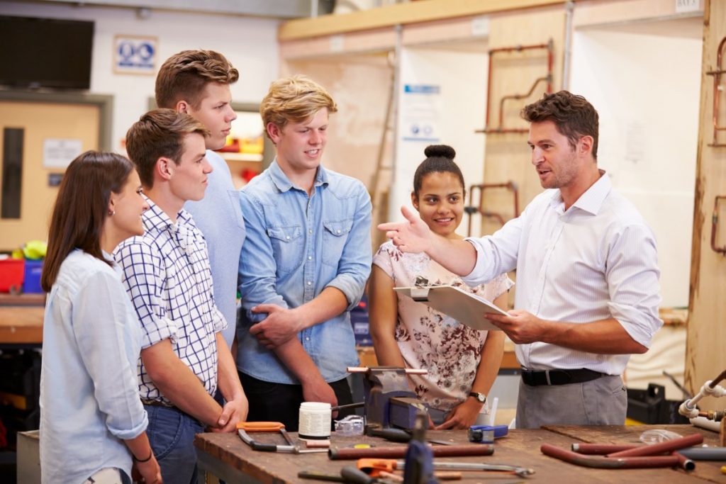 Ausbilder spricht mit einer Gruppe junger Auszubildender in einer Werkstatt – Symbolbild für Azubi-Workshop und Onboarding