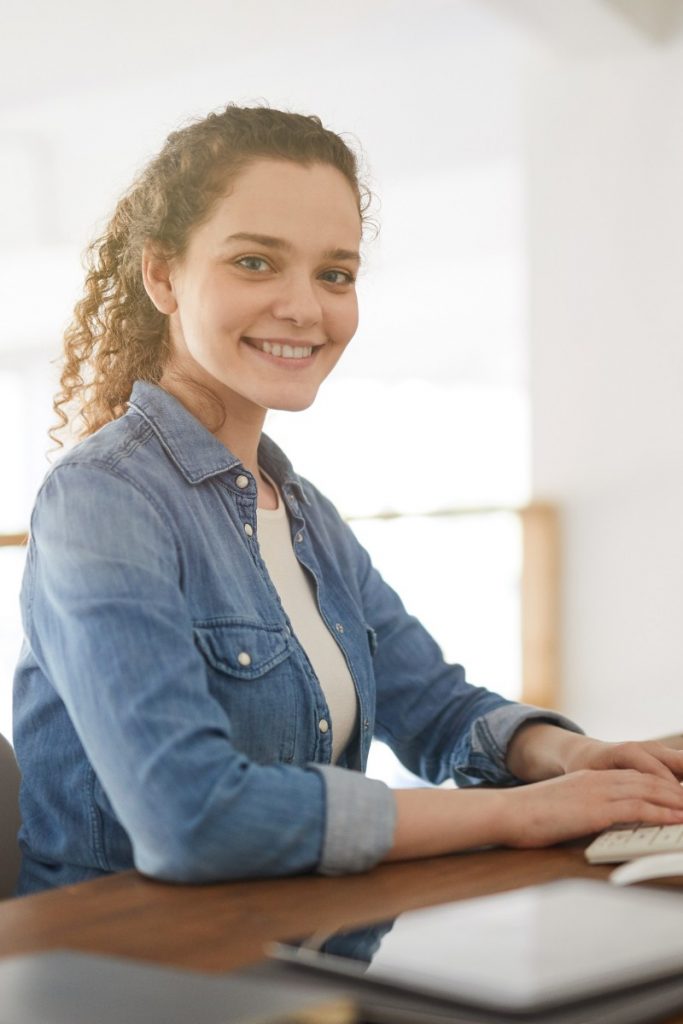 Junge Mitarbeiterin sitzt lächelnd am Computer und steht für Onboarding, Berufseinstieg und Ankommen im Unternehmen.