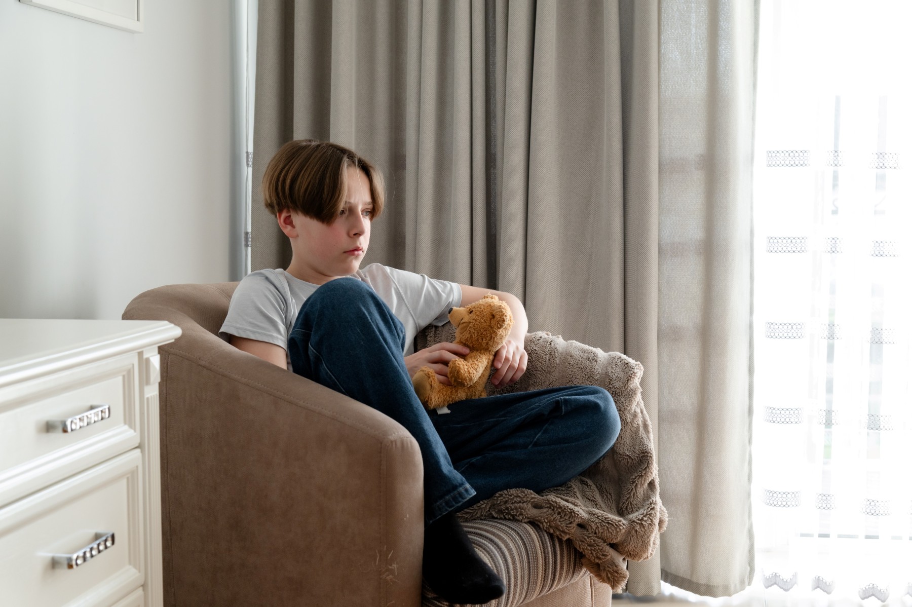 Nachdenkliches Kind sitzt mit einem Kuscheltier in einem Sessel
