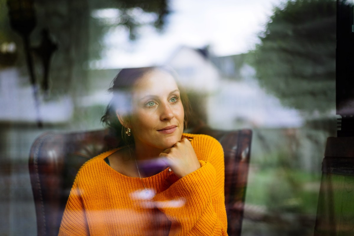 Nachdenkliche Frau sitzt hinter einer Fensterscheibe