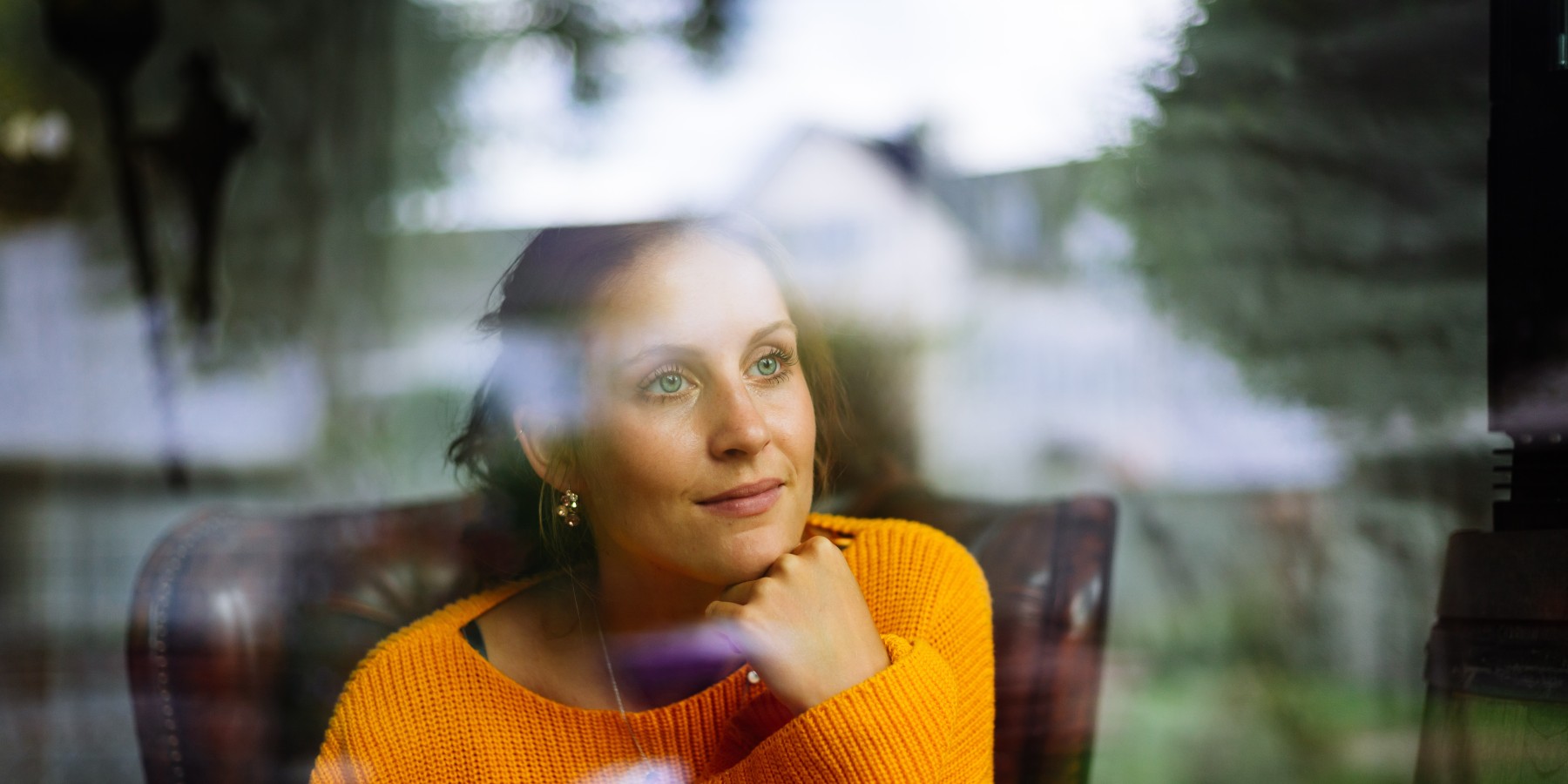 Nachdenkliche Frau sitzt hinter einer Fensterscheibe