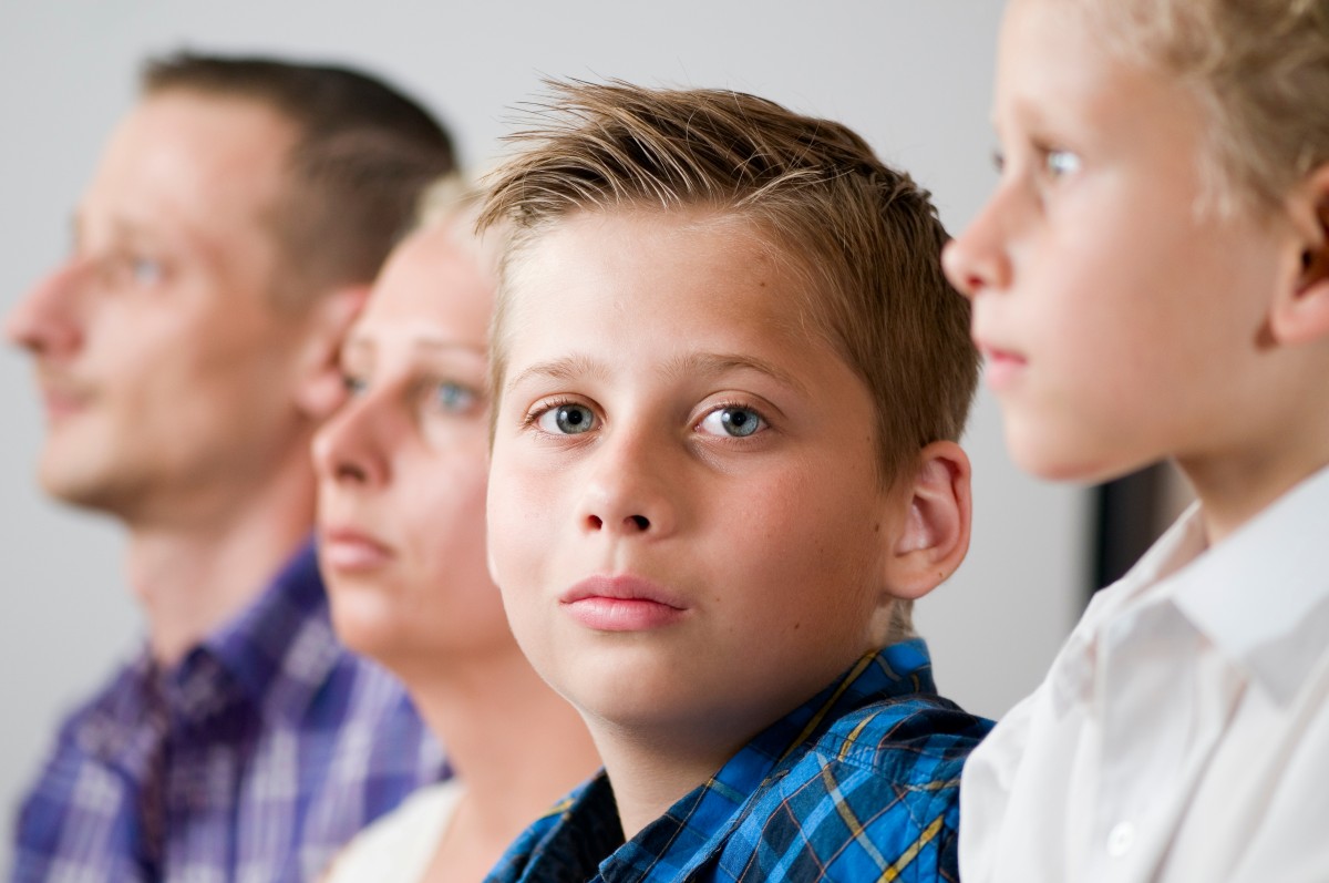 Nachdenkliches Kind sitzt zwischen zwei Erwachsenen